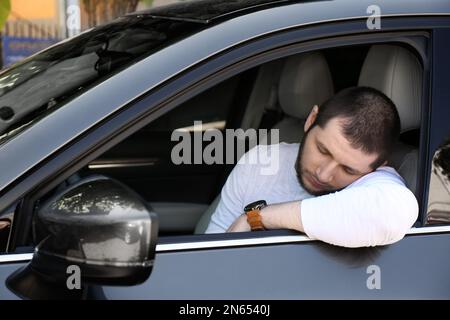 Homme fatigué dormant dans sa voiture moderne Banque D'Images