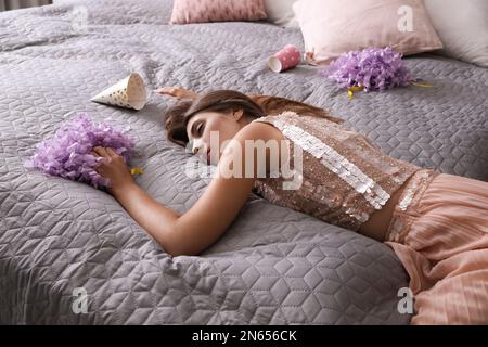 Femme épuisée en tenue de fête dormant sur le lit à la maison après la fête Banque D'Images