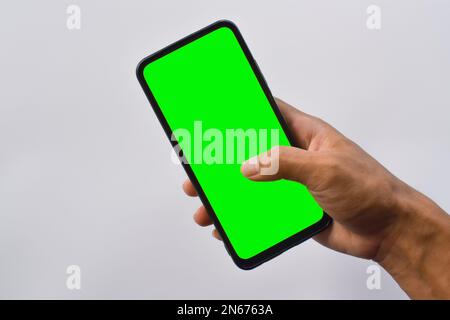 Modèle mobile. Main de l'homme tenant un smartphone noir avec écran vert en position verticale isolé sur fond blanc. Banque D'Images