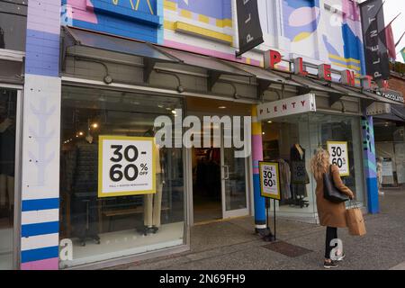 Une jeune femme portant un sac à provisions passe devant un grand magasin de vêtements pour femmes sur la rue Robson, au centre-ville de Vancouver, en Colombie-Britannique, au Canada Banque D'Images