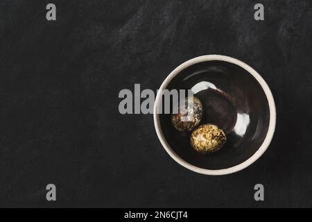 Œufs de caille frais bio gratuits dans un bol en céramique sur fond rustique noir. Vue de dessus. Banque D'Images