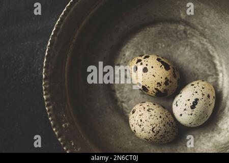 Œufs de caille frais bio gratuits dans un bol en cuivre sur fond rustique noir. Vue de dessus. Banque D'Images