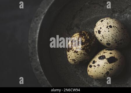 Œufs de caille frais bio gratuits dans un bol en pierre noire sur fond rustique noir. Vue de dessus. Banque D'Images