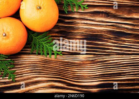 Les tangerines se rapprochent - sur une table en bois près des branches de conifères de genévrier. Arrière-plan de Noël. Arrière-plan de Noël. Vacances d'hiver. Mise à plat. Banque D'Images