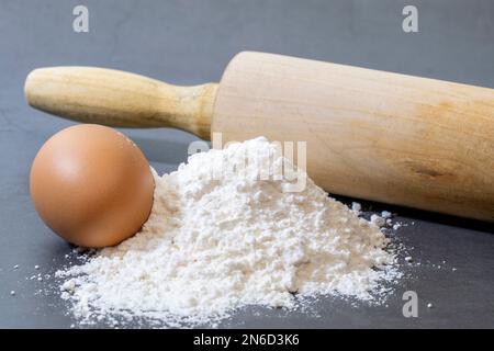 Tas de farine et d'œuf polyvalents pour faire du pain maison sur fond sombre. Banque D'Images