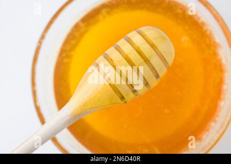 Balancier au miel dans un bol en bois avec du miel au soleil. Miel épais bio sain trempant d'une cuillère en bois de miel, gros plan. Banque D'Images