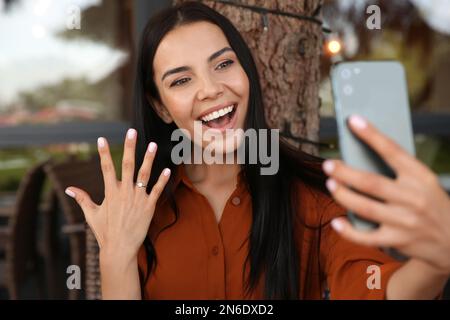 Une femme heureuse avec un anneau de fiançailles prenant le selfie dans un café en plein air Banque D'Images