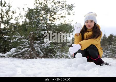 Jolie petite fille qui roule des boules de neige dans la forêt d'hiver Banque D'Images