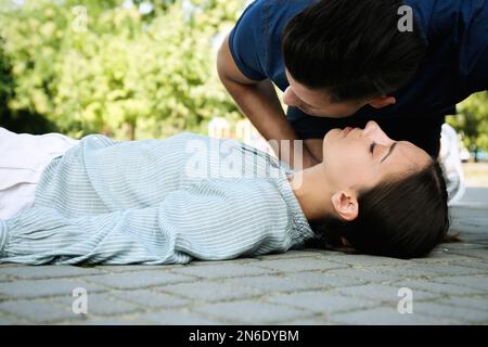 Homme vérifiant la respiration de la jeune femme inconsciente à l'extérieur Banque D'Images