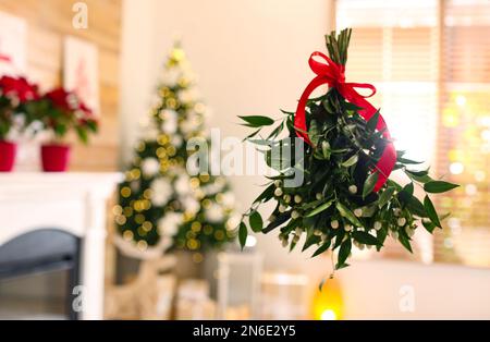 Bouquet de GUI avec noeud rouge suspendu dans la chambre décorée pour Noël, espace pour le texte Banque D'Images