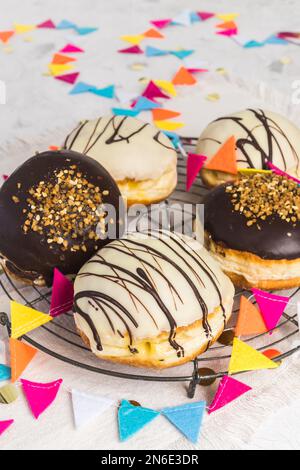 Pâtisseries berliners allemandes traditionnelles, émaillées de chocolat noir et blanc et de cassants noisettes, décorées pour la fête ou le carnaval, verticales Banque D'Images