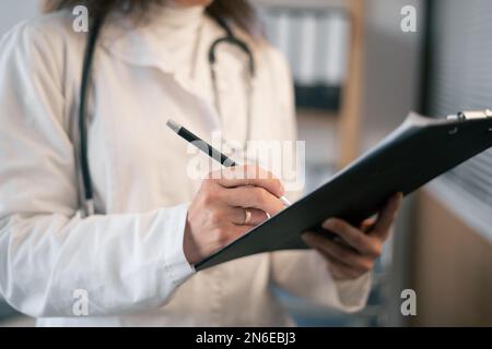 Gros plan des mains du médecin féminin avec le presse-papiers. Prendre des notes dans le presse-papiers pendant qu'il est à l'hôpital. Soins de santé antécédents médicaux. Services médicaux Banque D'Images