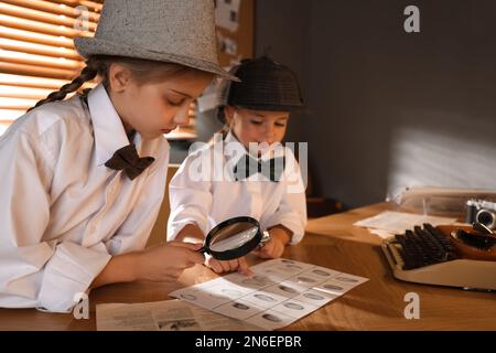 Jolis petits détectives explorant des empreintes digitales avec des loupes à la table dans le bureau Banque D'Images
