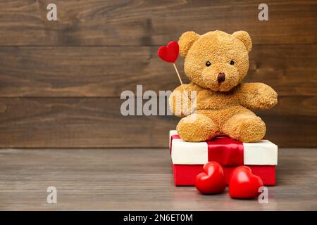 Adorable ours en peluche avec coeurs rouges et boîte cadeau sur table en bois, espace pour le texte. Célébration de la Saint-Valentin Banque D'Images