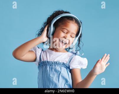 Adorable petite fille hispanique debout avec ses yeux fermés et regardant heureux tout en portant des écouteurs et en écoutant de la musique, dansant à elle Banque D'Images