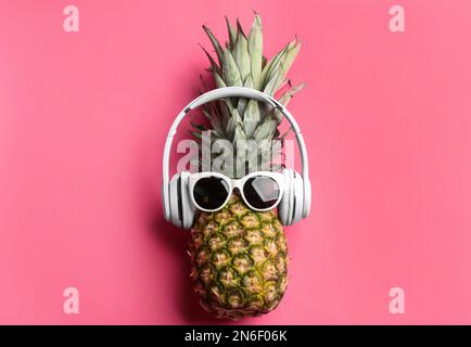 Ananas avec lunettes de soleil et écouteurs sur fond rose, vue du dessus. Concept créatif Banque D'Images