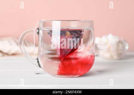 Sachet de thé dans une tasse en verre avec de l'eau sur une table en bois blanc Banque D'Images