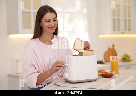 Jeune femme utilisant le grille-pain à la table dans la cuisine Banque D'Images