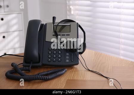 Téléphone fixe et casque sur une table en bois à l'intérieur. Service d'assistance téléphonique Banque D'Images