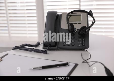 Téléphone de bureau avec micro-casque sur une table blanche au bureau. Service d'assistance téléphonique Banque D'Images