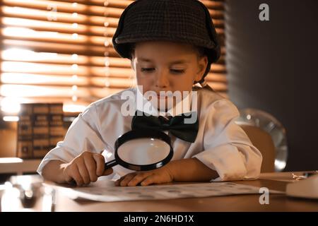 Joli petit détective explorant les empreintes digitales avec la loupe à la table dans le bureau Banque D'Images