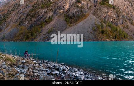 Une jeune pêcheur se trouve sur la rive du lac alpin Shavlinskoye parmi les pierres des rochers et attrape des poissons avec une canne à pêche dans l'Altaï Banque D'Images