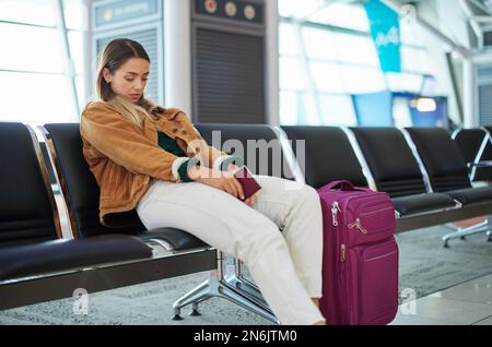 Femme ennuyée, aéroport et bagages en attente avec passeport pour vol, voyage ou voyage de vacances au Cap. Une femme en voyage fatiguée attend Banque D'Images