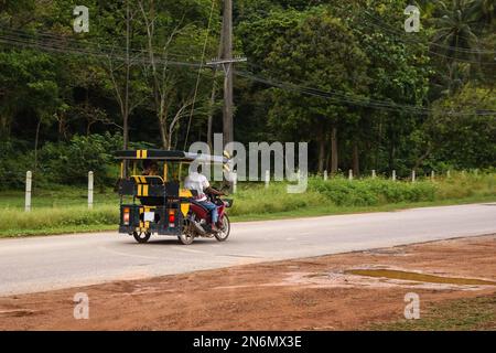 Tuk tuk taxi tuk dans la campagne de Thaïlande avec deux touristes à bord. Ko Lanta, Krabi. Banque D'Images