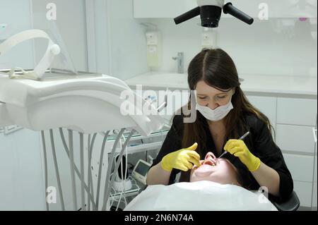 femme dentiste dans les gants jaunes et les vêtements noirs prothétique dents elle examine la patiente avec l'aide de miroir beaucoup de la technologie la plus récente whit Banque D'Images