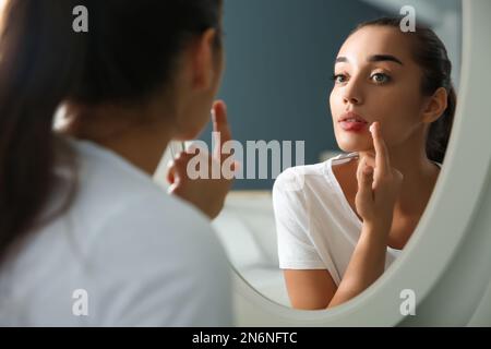 Jeune femme avec l'herpès appliquant de la crème sur les lèvres devant le miroir à la maison Banque D'Images