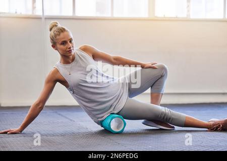 Fitness, physio et pilates, femme avec rouleau sur le sol pour la tension des jambes et le soutien dans l'entraînement de yoga à la salle de gym. Santé, sport et massage pour Banque D'Images