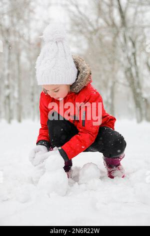 Jolie petite fille faisant des boules de neige à l'extérieur le jour de l'hiver Banque D'Images