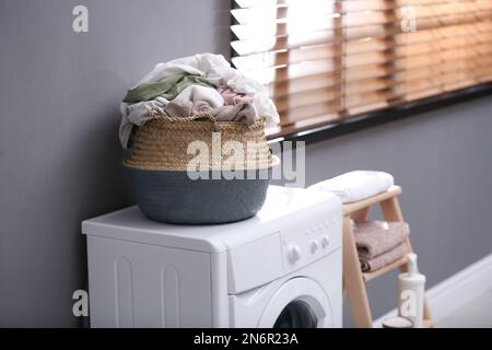 Panier en osier avec linge sale sur le lave-linge près du mur gris à l'intérieur Banque D'Images