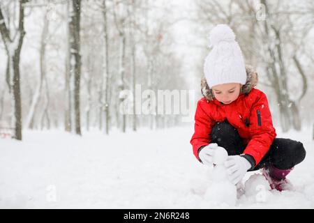 Jolie petite fille faisant des boules de neige à l'extérieur le jour de l'hiver, espace pour le texte Banque D'Images