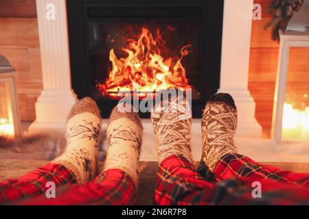 Couple en chaussettes chaudes reposant près de la cheminée à la maison, à proximité Banque D'Images