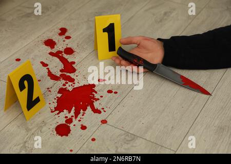 Marqueurs de scène de crime et corps mort avec couteau sanglant sur le sol, gros plan Banque D'Images