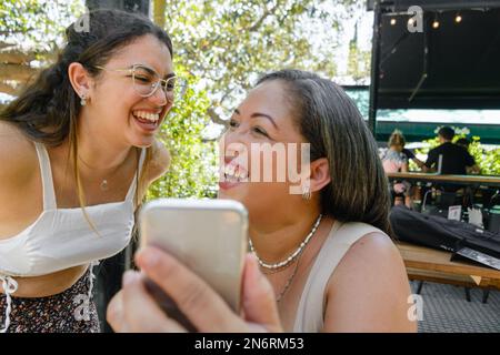 deux jeunes latines d'origine vénézuélienne, mère et fille, se réjouiront de regarder les réseaux sociaux au téléphone, assis dans un restaurant. Banque D'Images