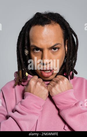portrait d'un homme multiracial percé à capuche rose regardant un appareil photo isolé sur le gris Banque D'Images