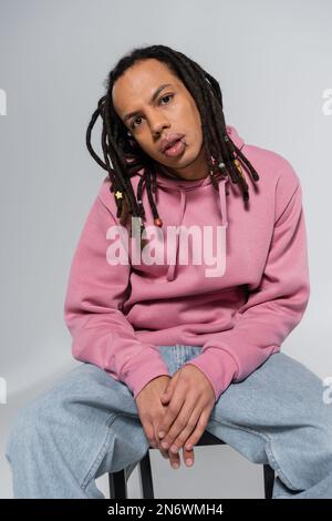 homme multiracial et percé avec des dreadlocks regardant la caméra tout en étant isolé sur le gris Banque D'Images