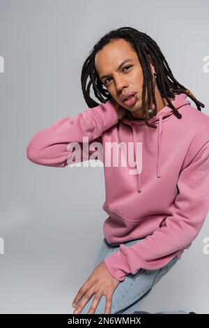 homme multiracial percé avec des dreadlocks regardant la caméra et posant sur le gris Banque D'Images