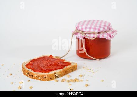 Sauce au piment et au poivre de tomate avec une tranche de pain et un petit pot en verre isolé sur fond blanc. Banque D'Images