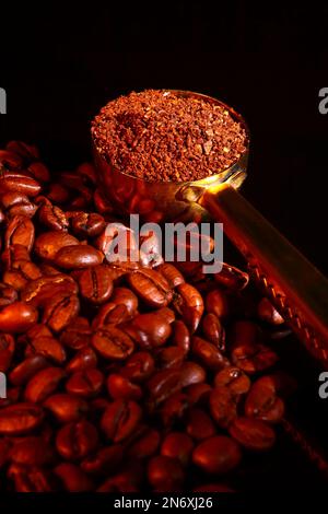 Grains de café torréfiés et une cuillère à café remplie de grains de café fraîchement moulus isolés sur un verre noir Banque D'Images