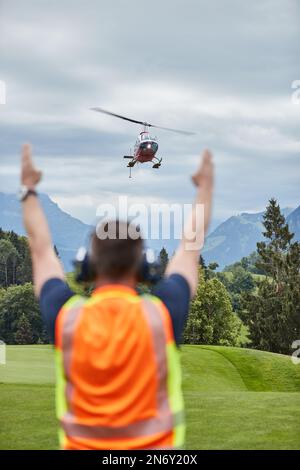 Homme de derrière instruisant un hélicoptère dans le processus d'atterrissage dans les Alpes suisses Banque D'Images