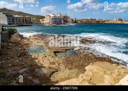 Baie de Qbajjar, Gozo - 13 octobre 2020 : marmites de sel avec la batterie de Qolla l-Bajda en arrière-plan. Banque D'Images