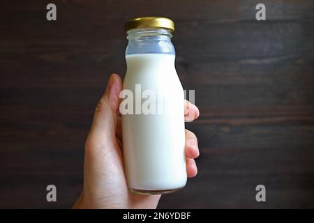 Bouteille de lait en verre à la main contre un mur en bois noir Banque D'Images