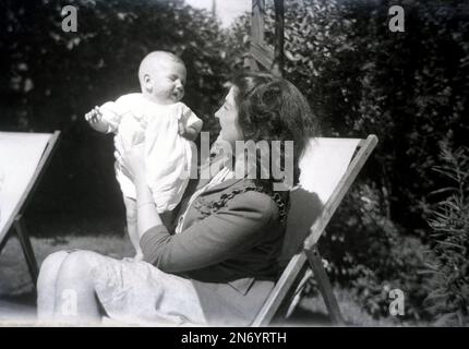 Années 1940, historique, été, une mère assise dans un transat dans un jardin arrière tenant son bébé, Angleterre, Royaume-Uni. Banque D'Images