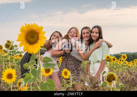 Quatre adolescentes dans un champ de tournesols en fin d'après-midi d'été, avec une grande fleur de tournesol au premier plan. Copier l'espace. Banque D'Images