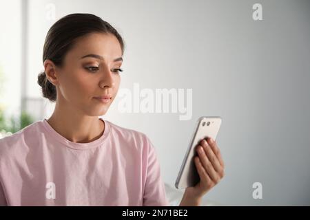 Jeune femme déverrouillant un smartphone avec un scanner facial à l'intérieur. Vérification biométrique Banque D'Images