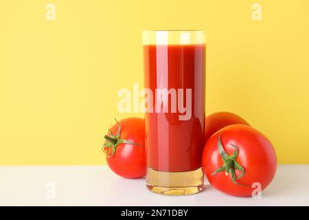 Verre de jus délicieux et tomates fraîches sur table blanche sur fond jaune, espace pour le texte Banque D'Images