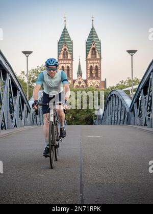 Cycliste à Fribourg. Sur le 'Blue Bridge', qui est fermé à la circulation routière. En arrière-plan, la Stühlinger Kirchplatz avec les deux tours de l'église du Sacré-cœur. Banque D'Images